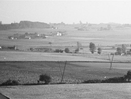 I forgrunden anes Ugledigevej. Dernæst Maglebjerggård, der i 1932 måtte afgive jord til anlæggelsen af den nye del af Ørslevvej. Bag gården ses Ørslevvej og nogle af de huse der skød op langs med vejen. Sylvest Jensen luftfoto 1956. Det Kongelige Bibliotek.